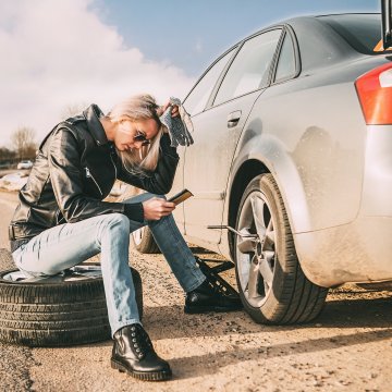 extended car warranty woman sitting on tire with phone in hand car breakdown open trunk USAA 